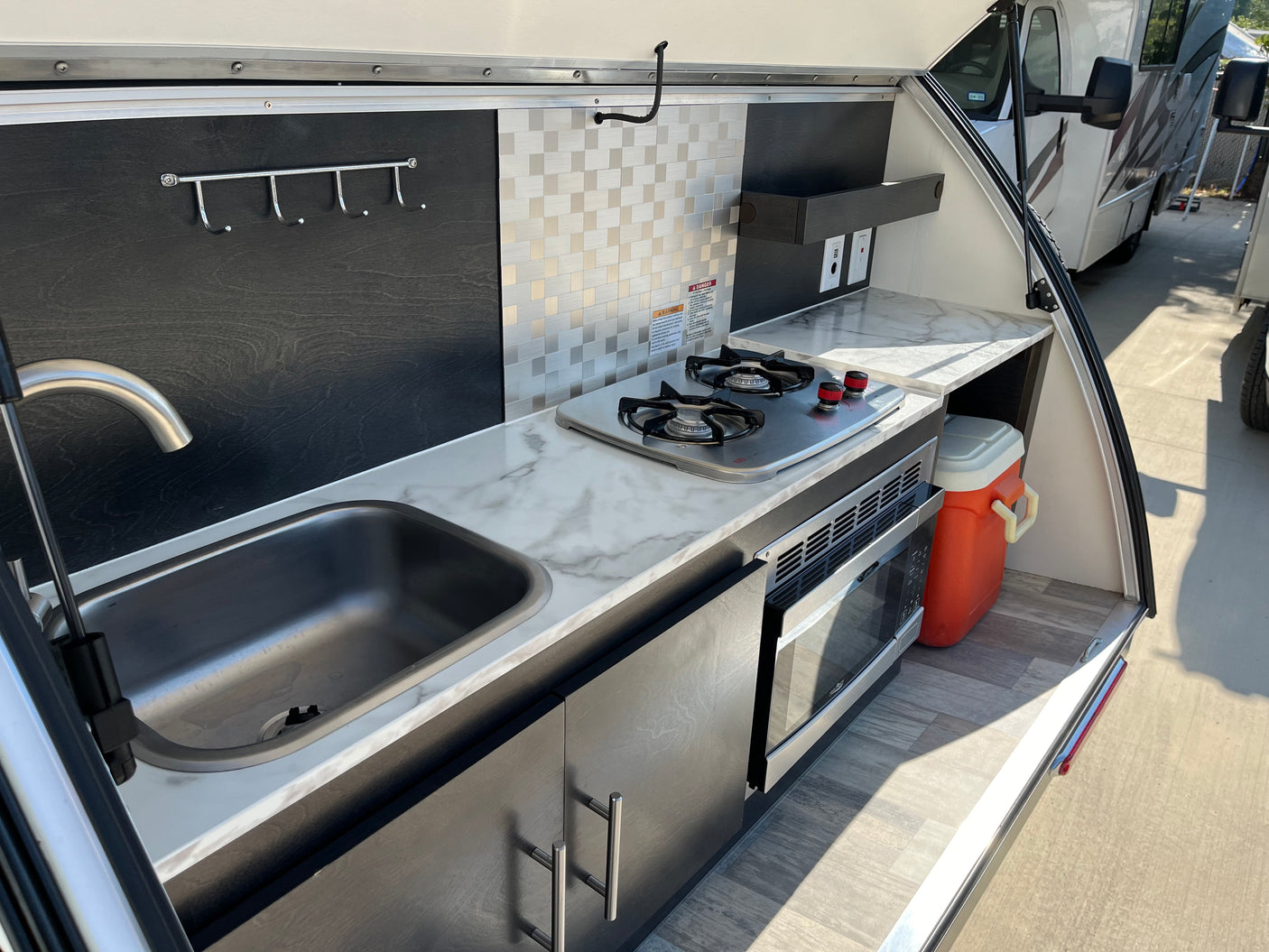 Explore this RV rental's clever outdoor galley: sink, stovetop, microwave, and cooler, perfect for camp cooking.