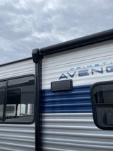 White & blue rv rental exterior: corrugated siding, dark windows, & black awning against a cloudy sky. Ready for travel.