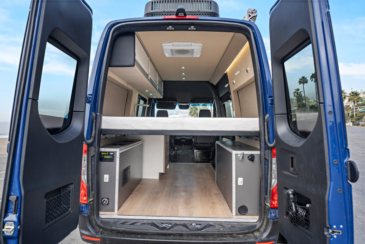 Rear view of an RV rental with open doors, revealing a spacious camper van interior featuring a bed, kitchen, & storage. — photo 5