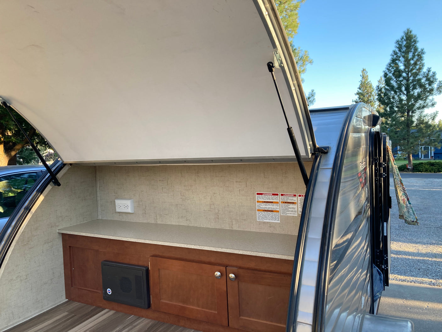 Inside an RV rental's open outdoor kitchen, featuring a counter, cabinets, and power outlet, perfect for camping.