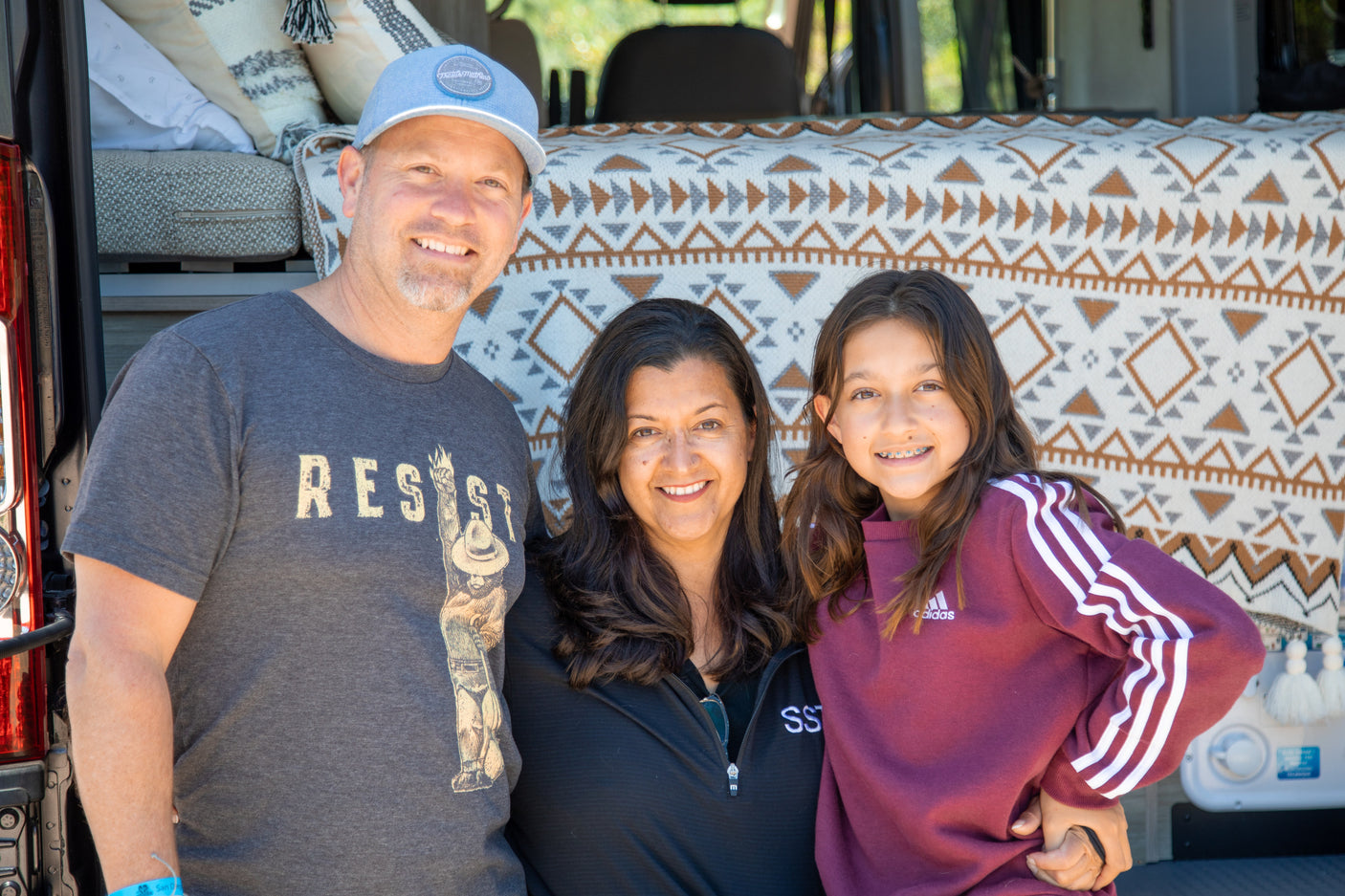 Smiling family of three by their RV rental, showcasing a cozy bed setup inside.