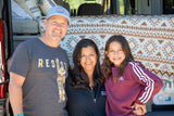 Smiling family of three by their RV rental, showcasing a cozy bed setup inside.