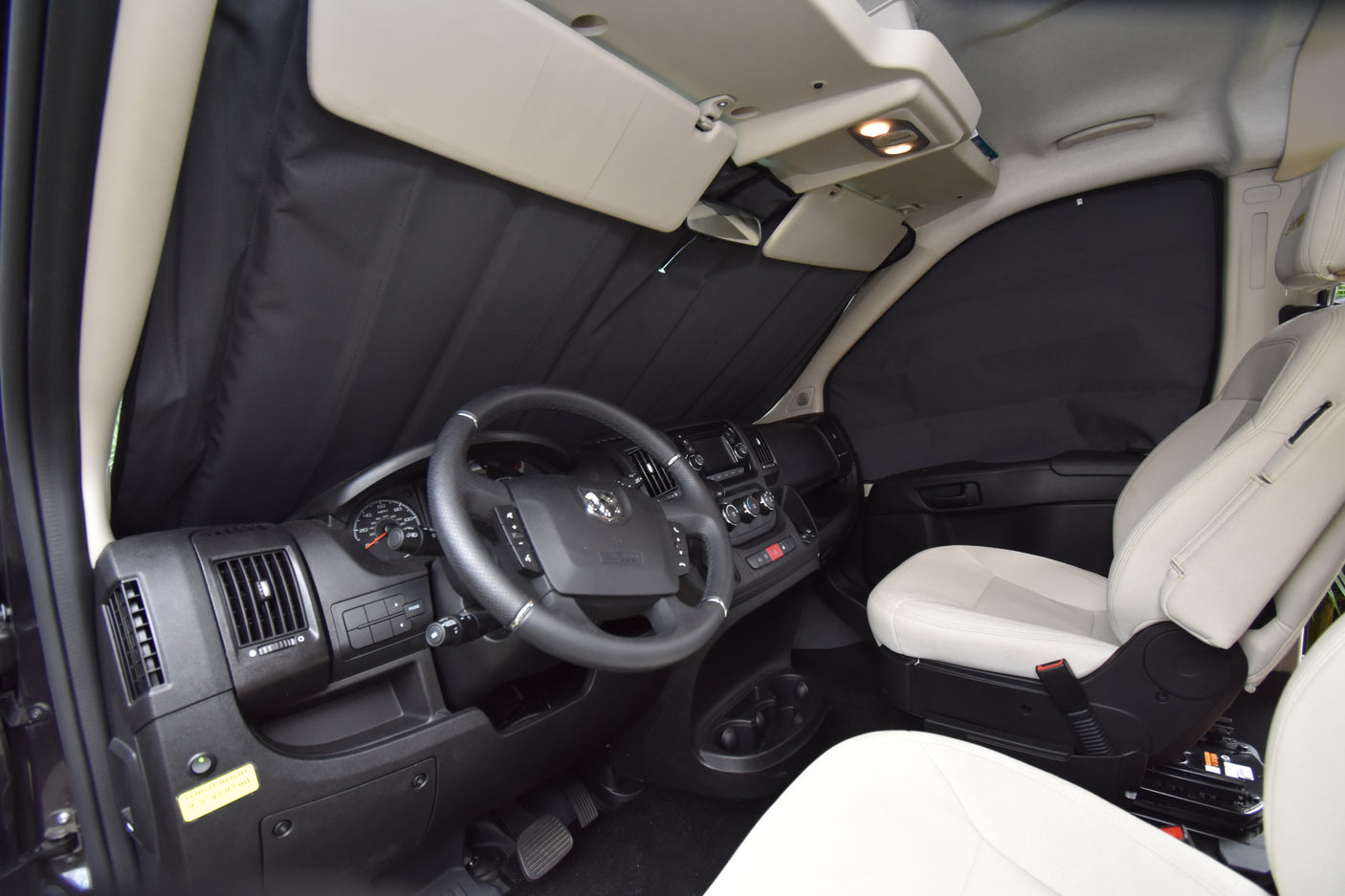 RV rental driver's cabin with black privacy shades on windows, showing dashboard, steering wheel, and light seats.