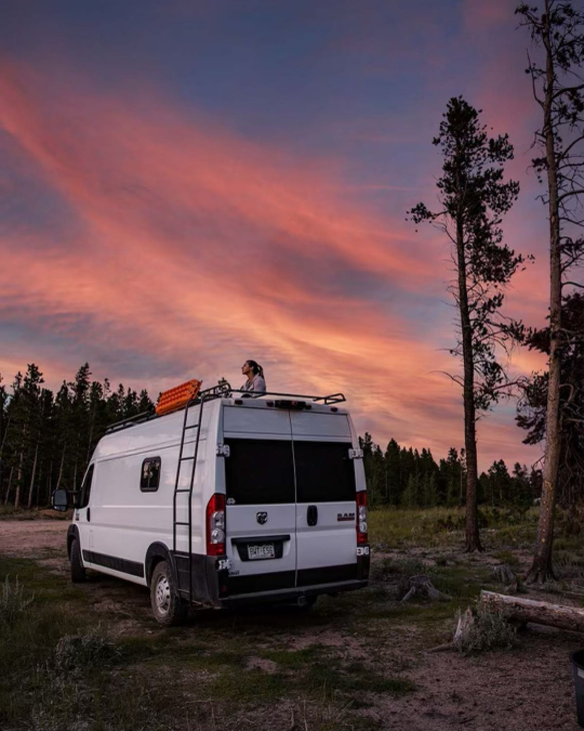 Serene sunset from an rv rental. A person watches the vibrant sky from atop a white camper van