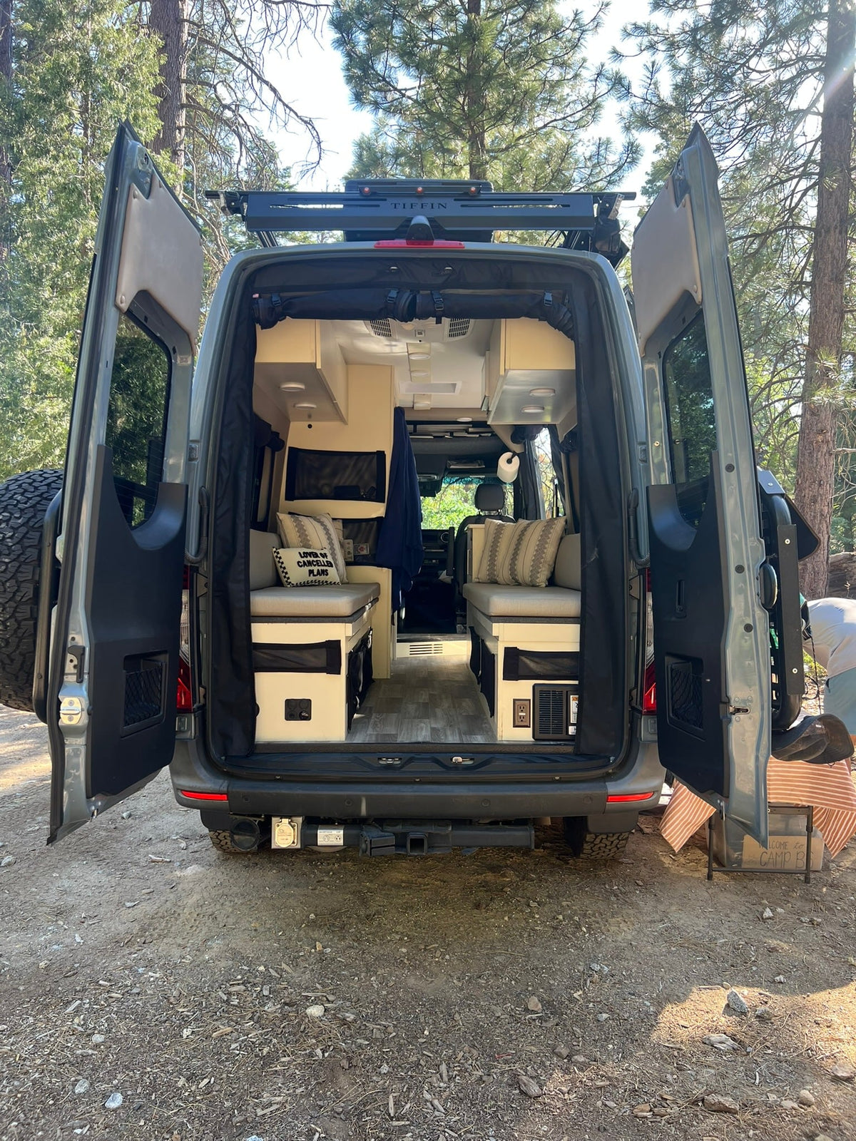  showcasing cozy seating/bed areas and storage in a peaceful forest setting.|This RV rental features a compact kitchen with an induction cooktop & sink — photo 5