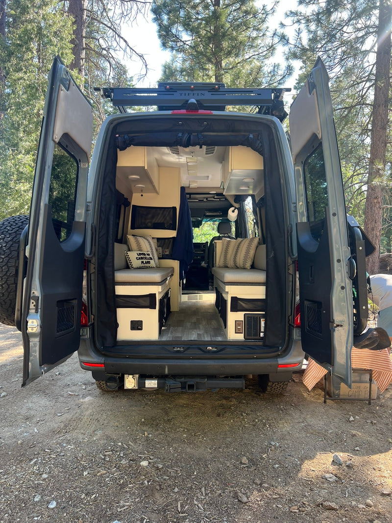  showcasing cozy seating/bed areas and storage in a peaceful forest setting.|This RV rental features a compact kitchen with an induction cooktop & sink — photo 5