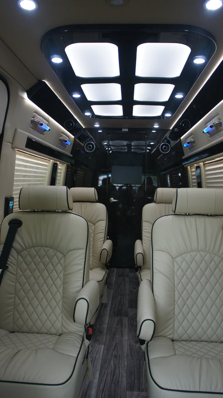 Spacious RV rental interior: Cream quilted leather seats, bright overhead lighting, and entertainment. Experience luxury travel.