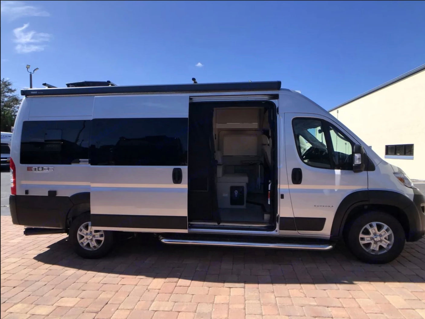 Silver camper van rv rental parked with its side door open, revealing the interior. An awning is extended above the door.