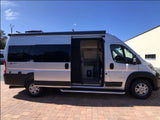 Silver camper van rv rental parked with its side door open, revealing the interior. An awning is extended above the door.