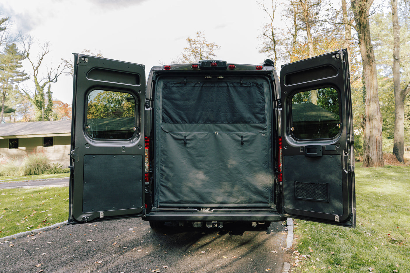 Discover this RV rental van with its rear doors open, revealing a blackout privacy screen and organized interior.