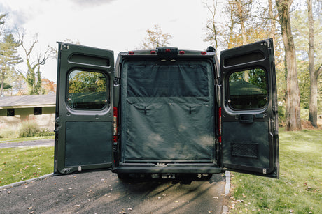 Discover this RV rental van with its rear doors open, revealing a blackout privacy screen and organized interior.