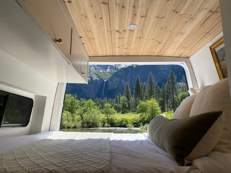 Wake up to nature! This RV rental's cozy camper bed offers stunning views of a river, forest, & waterfall. — photo 1