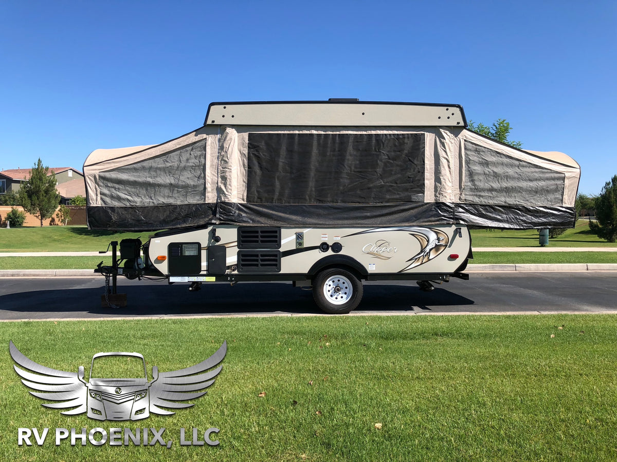 A beige and grey pop-up camper for RV rental, fully extended and parked on asphalt next to green grass under a clear sky.