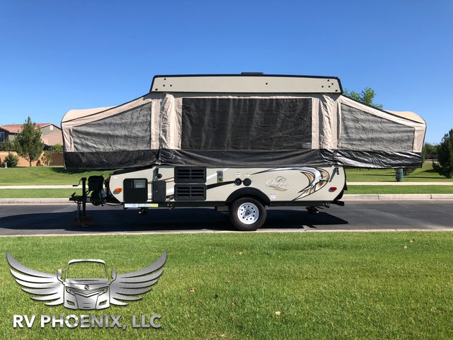 A beige and grey pop-up camper for RV rental, fully extended and parked on asphalt next to green grass under a clear sky.