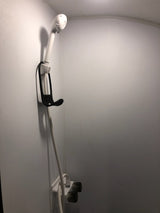 RV rental compact shower: white handheld showerhead on a wall mount with a black strap, hose, and water knobs below.