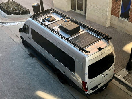 Silver Airstream camper van with roof rack, solar panels, and AC unit, potentially an rv rental, parked on a street.
