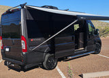 Black camper van with an extended awning parked on gravel. Ideal for rv rental adventures in desert landscapes.