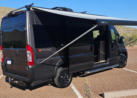 Black camper van with an extended awning parked on gravel. Ideal for rv rental adventures in desert landscapes.