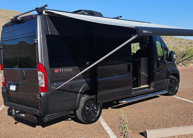  ready for a desert road trip.|A dark grey camper van with an extended awning is parked in a desert landscape — photo 9