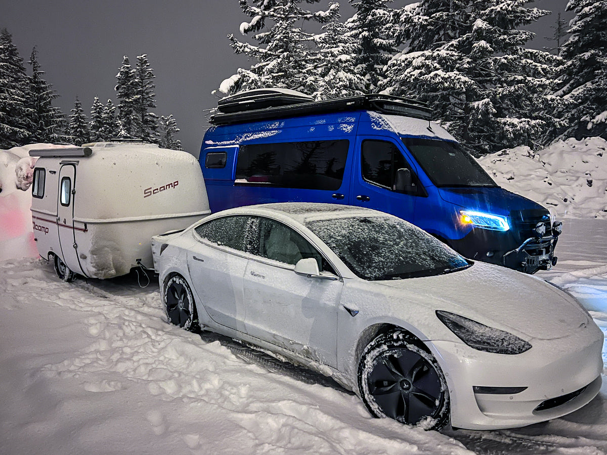 Snow-covered Tesla towing a Scamp camper, parked next to a blue van, ready for a winter rv rental trip. — photo 5