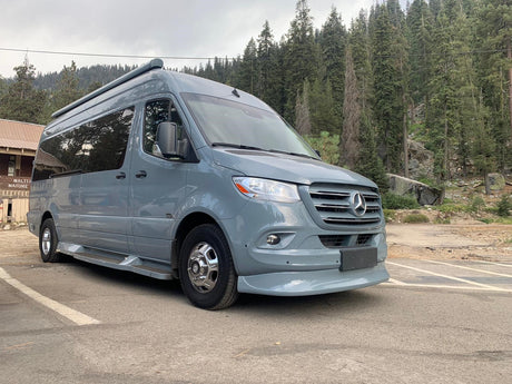 A sleek grey Mercedes-Benz Sprinter RV rental parked in a scenic forest area, ready for outdoor adventures.