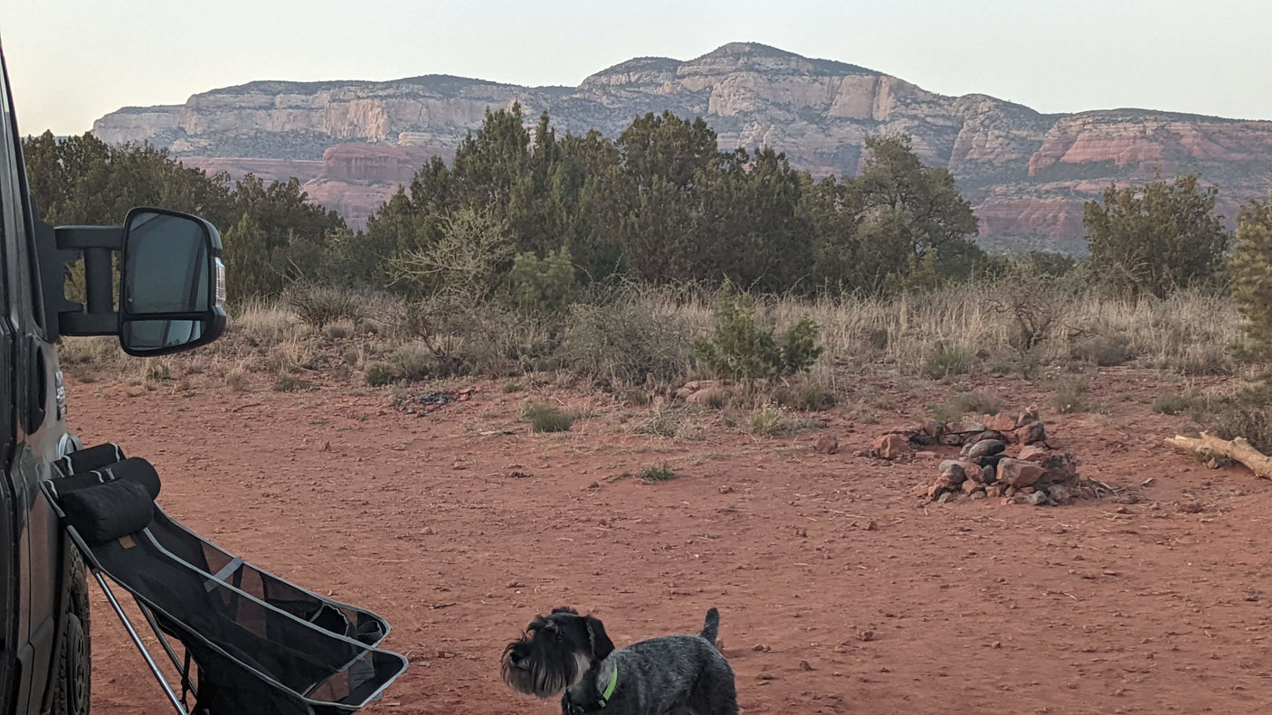 RV rental camping in the desert: A dog, chairs, & fire pit at a scenic spot with distant red rock mountains.