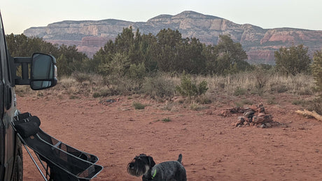 RV rental camping in the desert: A dog, chairs, & fire pit at a scenic spot with distant red rock mountains.