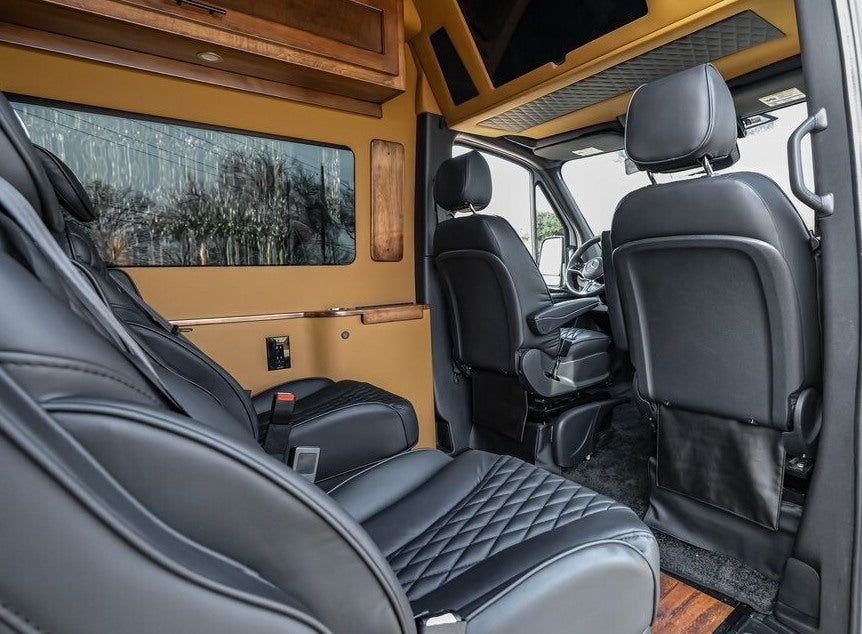 Premium RV rental interior with black quilted leather captain's chairs, elegant wood cabinetry, and a comfortable design. — photo 12
