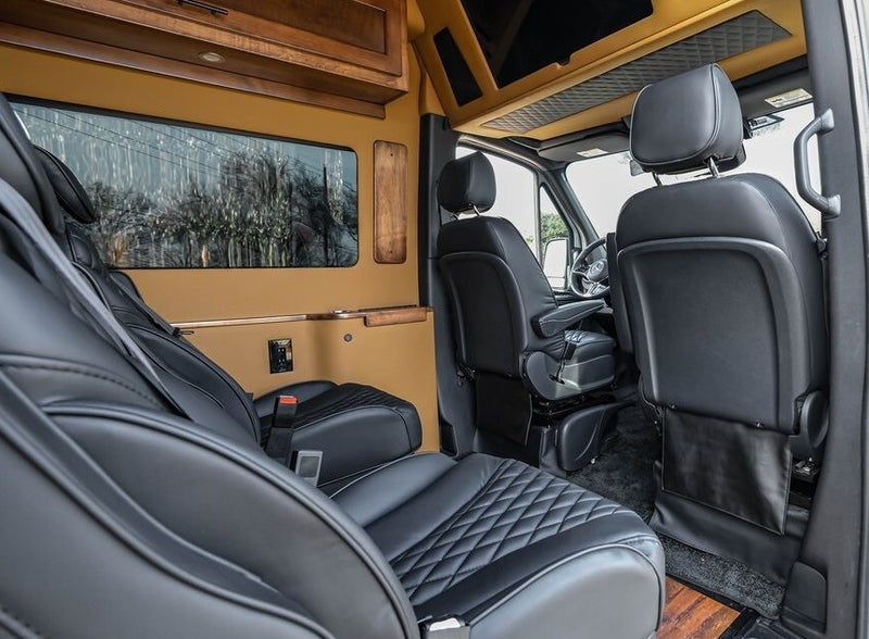 Premium RV rental interior with black quilted leather captain's chairs, elegant wood cabinetry, and a comfortable design. — photo 12