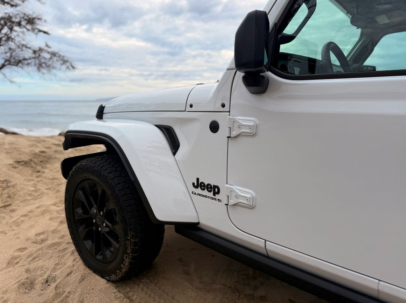 White Jeep Gladiator on a sandy beach, ocean in background. Rent this rugged 4x4 for your next RV rental adventure.