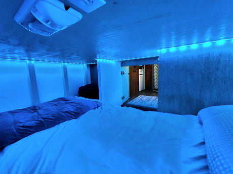 Cozy RV rental sleeping nook with blue LED strip lights illuminating the bed and interior.