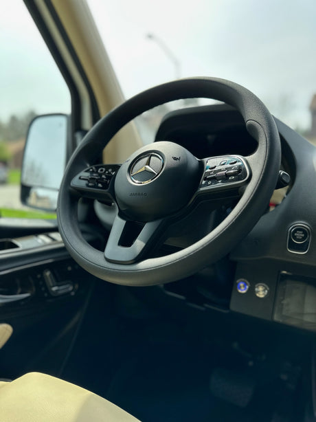 Inside your RV rental: a clear view of the Mercedes-Benz steering wheel and dashboard, highlighting controls and start button.
