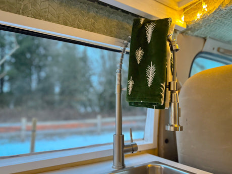 Cozy RV rental kitchen setup: Features a modern sink, a green towel, and a cold winter view outside.