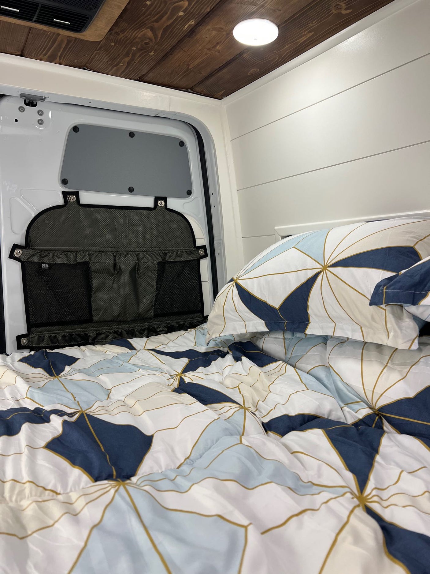 Inside a cozy RV rental: comfy bed with unique linens, plus smart storage on the back door for organized travel.