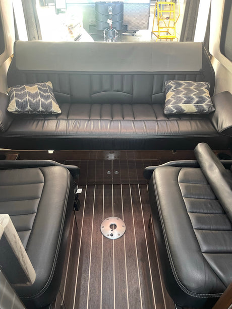 Spacious RV rental interior with comfortable black leather sofa, matching captain's chairs, and a sleek wood floor, ready for your road trip comfort.