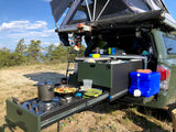 Green truck with pull-out kitchen & rooftop tent: cooking fresh veggies outdoors. Perfect for adventurous RV rental camping!