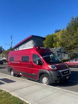 Red Winnebago Solis **rv rental** parked on a sunny street with pop-top open. This vibrant camper van is ready for adventure.