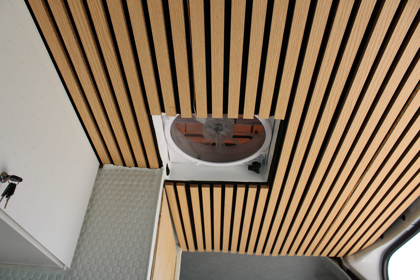Overhead view of an RV rental interior: slatted wooden ceiling, central vent fan, and white wall with keys.