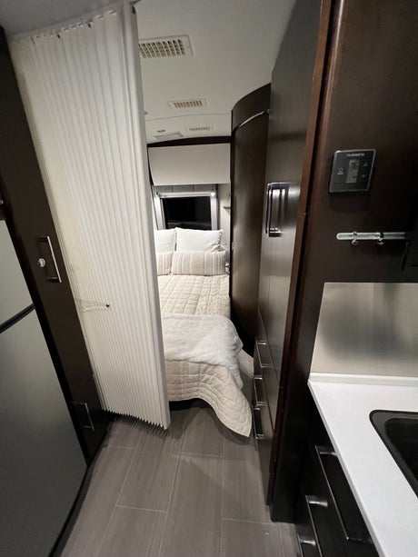 Inside an rv rental, a compact bedroom with quilted bedding is partially visible behind a white privacy curtain, next to a kitchen.