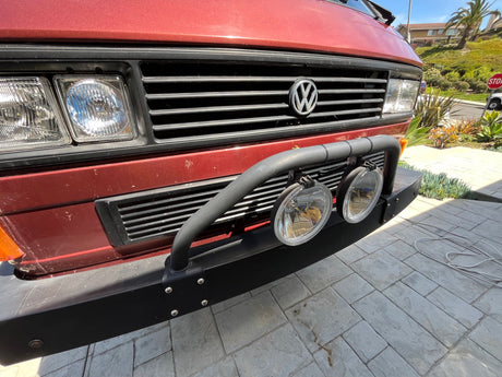 Red VW van, great for RV rental. Front view: classic black grille, square headlights, rugged bumper, and auxiliary lights.
