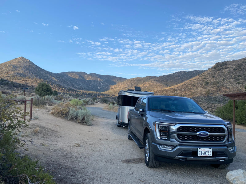 A grey Ford F-150 tows an RV rental trailer on a dirt road in a scenic mountain landscape, ready for adventure. — photo 13