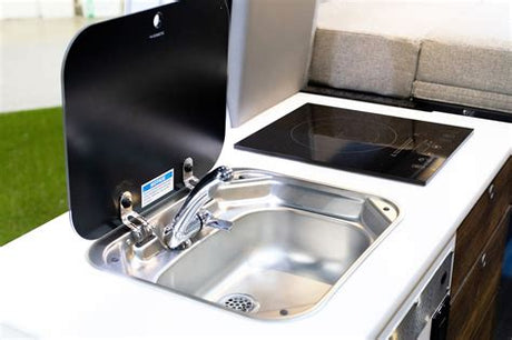 Visually impaired users: A compact RV rental kitchen features a Dometic sink with a flip-up cover and an electric cooktop.