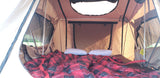 Cozy rooftop tent interior for RV rental adventures. Plaid blanket, pillows, and mesh windows offer comfort with an outdoor view.