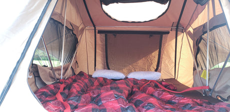 Cozy rooftop tent interior for RV rental adventures. Plaid blanket, pillows, and mesh windows offer comfort with an outdoor view.