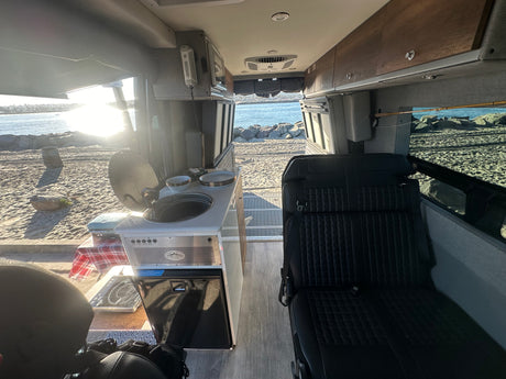Storyteller Overland RV rental interior with kitchen, seating, & beach view. Perfect for van life adventures by the ocean.