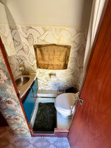 Stylish RV rental bathroom with gold ginkgo leaf wallpaper, blue vanity, sink, toilet, and shower curtain.