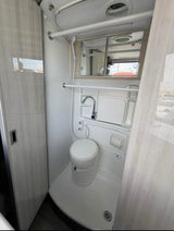 RV rental's compact bathroom: toilet, sink, shower, and mirror. Efficient, all-in-one design for travel adventures.