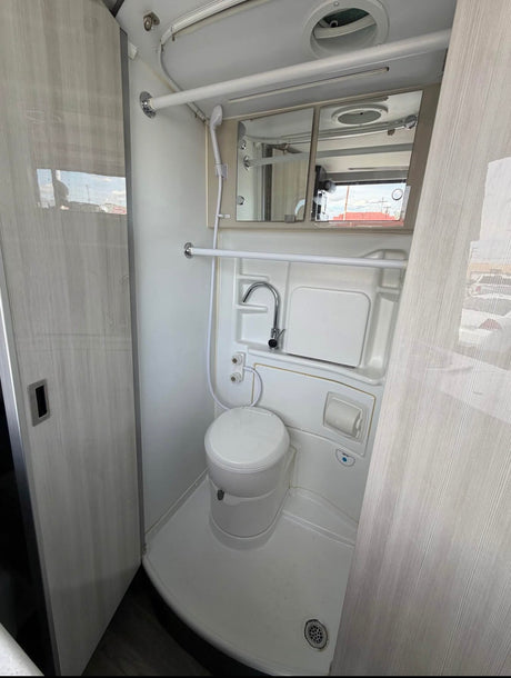 RV rental's compact bathroom: toilet, sink, shower, and mirror. Efficient, all-in-one design for travel adventures.