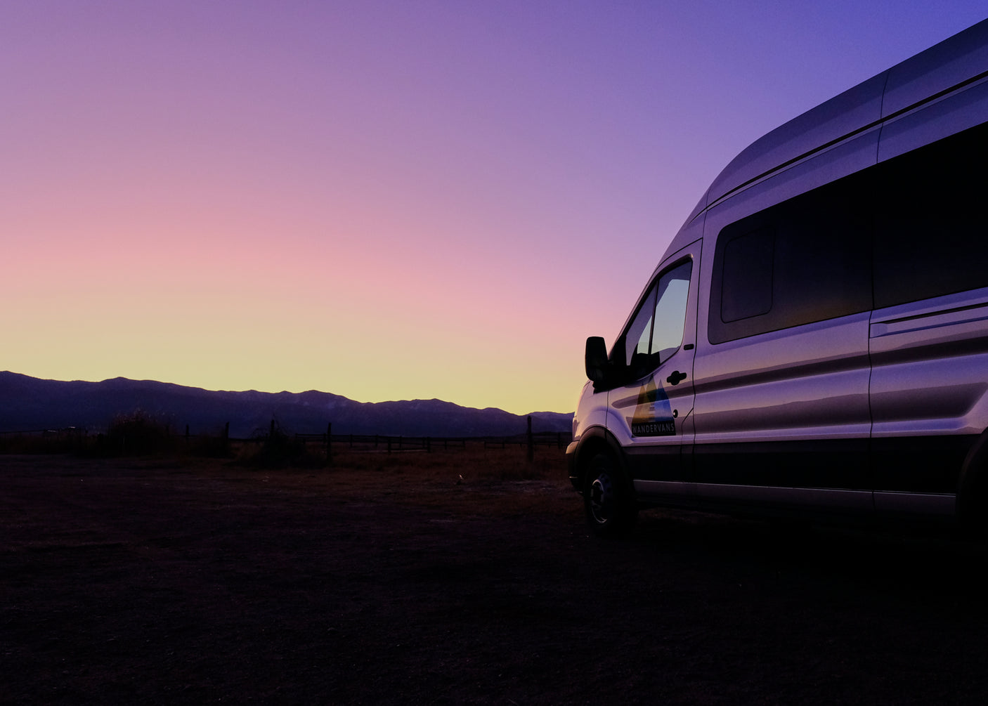 RV rental adventure: a WanderVans camper van parked at dusk, showcasing silhouetted mountains and a vibrant sky.