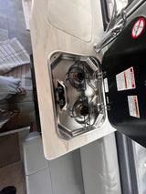 RV rental's compact kitchen with two-burner stove, sink, and faucet. Stove lid open, showing safety warnings.